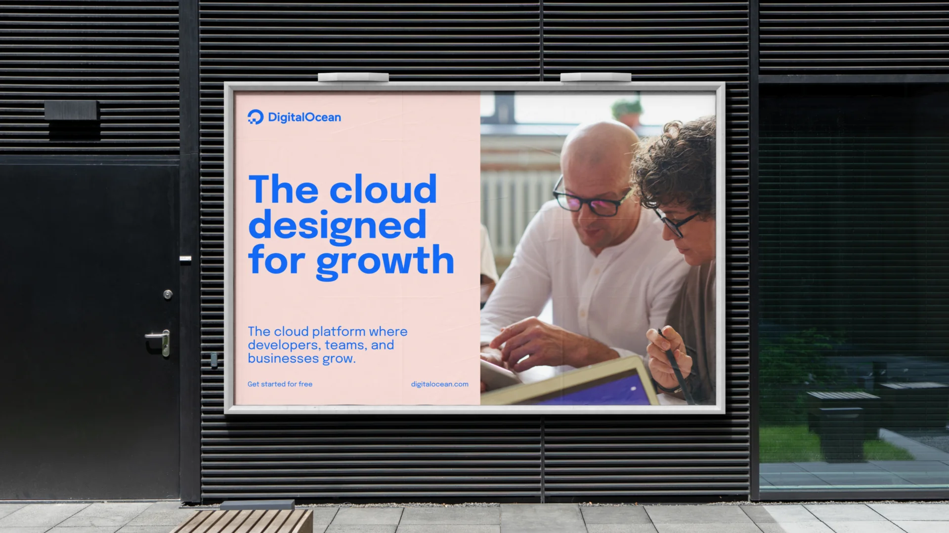 A DigitalOcean 'The cloud designed for growth' banner mounted on a building facade, above a photo of two people reviewing work together.