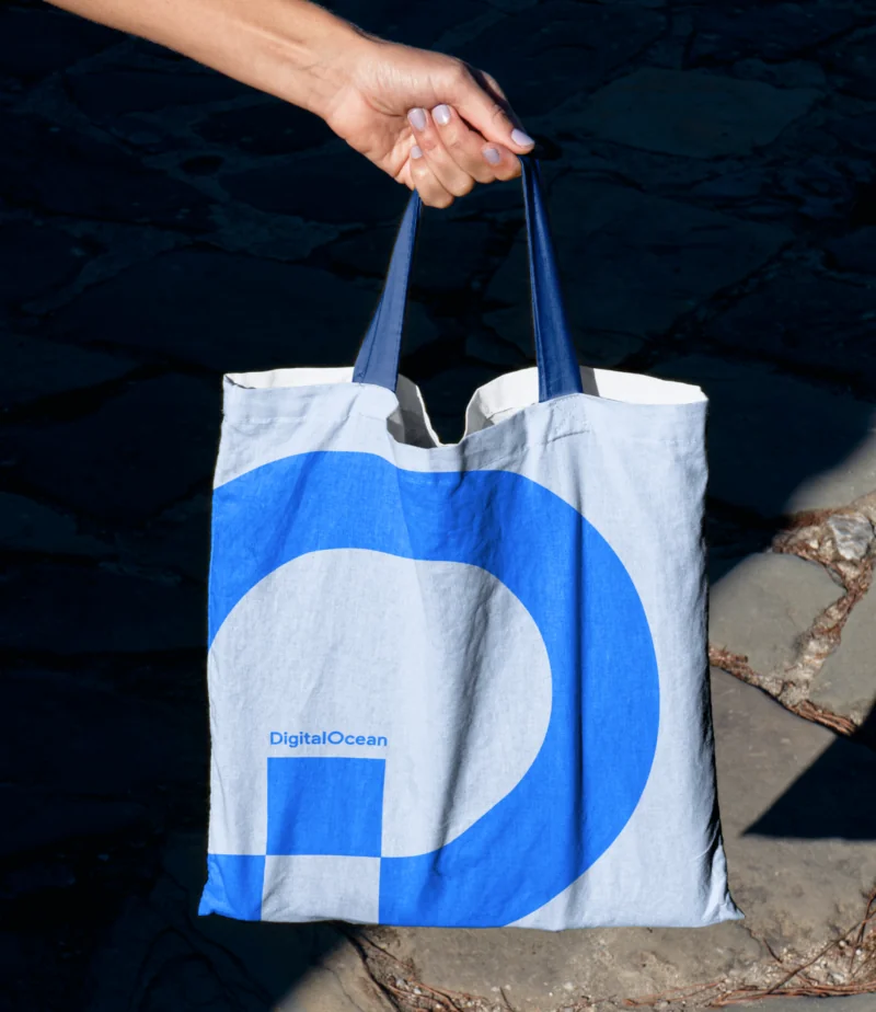A DigitalOcean tote bag, printed with the brand's dolphin mark in blue and gray, held outdoors in natural light.