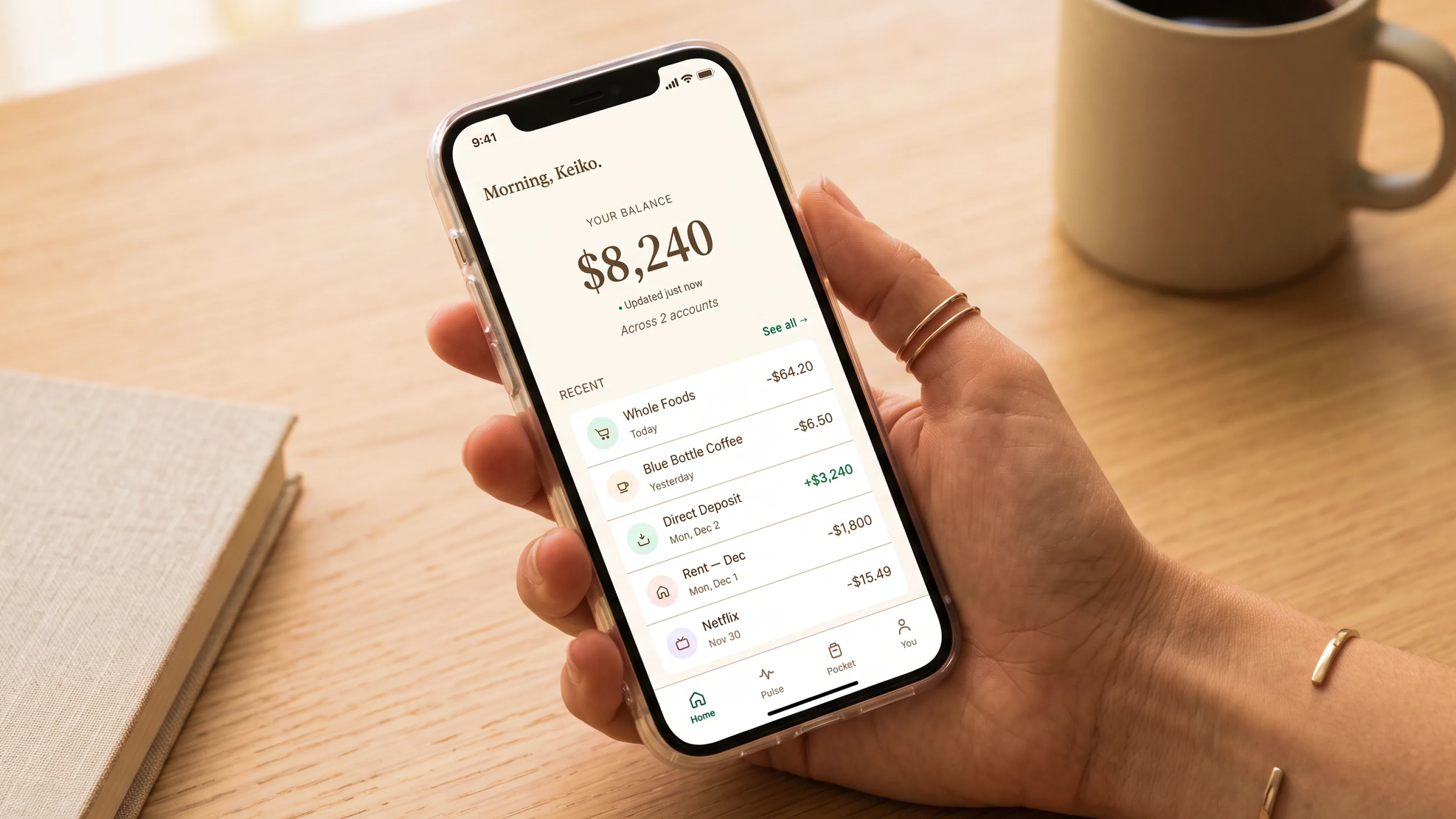 Folio personal finance app shown on real devices in a calm desk setting, with a balance dashboard, account list, recent activity, and gentle spending insight.