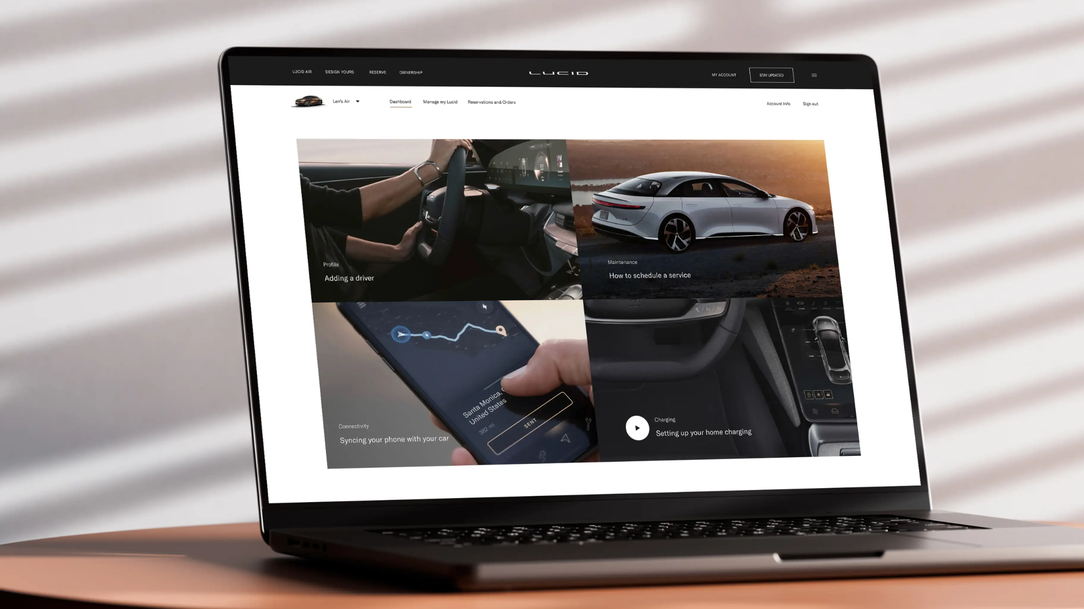 The Lucid ownership dashboard on a laptop — an owner's account with cards for adding a driver, scheduling service, syncing a phone with the car, and setting up home charging.