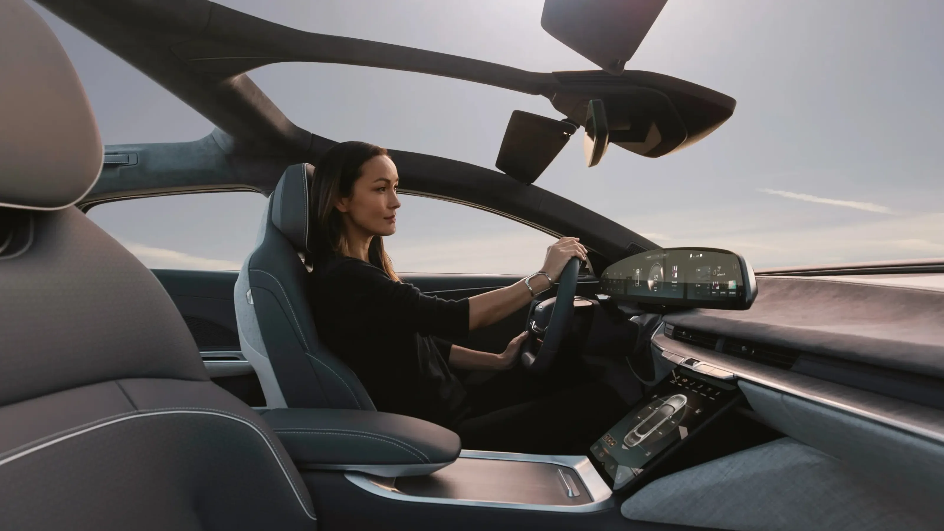 Interior of the Lucid Air — a driver at the wheel beside the curved cockpit display, cabin bathed in evening light, conveying refined luxury and precision.